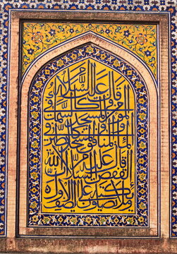 View of intricate Islamic calligraphy set against vibrant yellow and blue floral tilework, a cultural tapestry of faith and artistry, Lahore, Punjab, Pakistan.