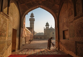 Lahore, Pakistan - 25 November 2017: View of the Wazir Khan Mosque's intricate brickwork and towering minarets framed by the ornate archway of Dehli Gate.