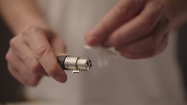 Sound engineer hands cleaning XLR audio cable connector with white cloth, performing maintenance on professional studio equipment for optimal performance and signal integrity.