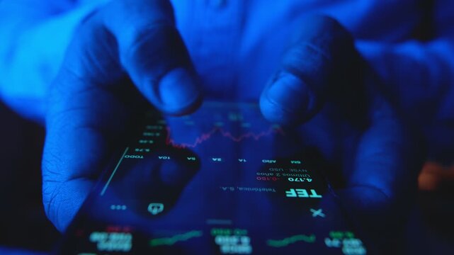 Closeup of a trader's hands scrolling through stock market charts on a mobile phone at night