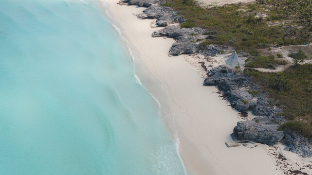 Aerial view of the white sand beach meeting the turquoise sea, with rocky outcrops and sparse vegetation providing contrast, Alice Town, Bimini, The Bahamas.