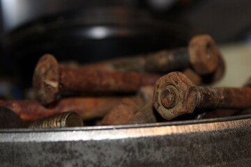 Rusty bolts and screws in a bowl in a workshop with tools and machinery in the background during daylight hours