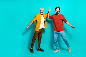 Obraz premium Two men high five in a bright teal studio showing friendship family bond and joyful wellness lifestyle for stock photography senior and younger generations