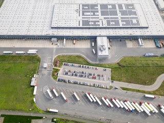 Top down aerial view of a logistics warehouse with loading docks, parked trucks and cars, showing organized transport infrastructure and supply chain operations