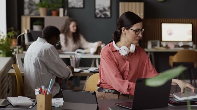 Medium shot of brunette woman saying goodbye and ending online conference, putting off wireless headphones. She taking paper folder and giving it to African American colleague
