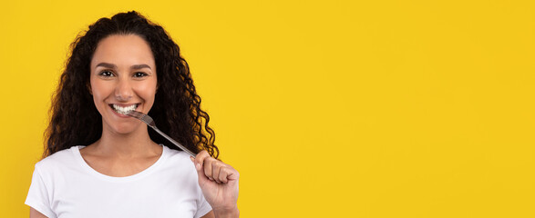 A woman with curly hair and a big smile is holding a fork near her mouth. She is wearing a white...