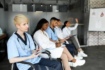 Obraz premium International group of doctors men and women different ages in workwear sitting on chairs, listening to speaker, taking notes, having professional training, copy space. Medical conference concept