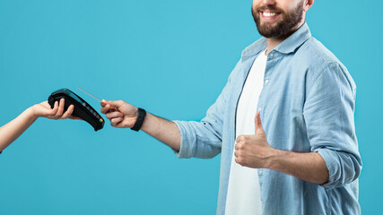 A man stands against a bright blue background, smiling as he completes a contactless payment using...