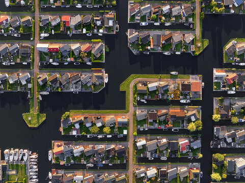 Aerial view of tightly packed homes with vibrant red roofs and lush green gardens nestled along the dark, winding canals., Lemmer, Friesland, Netherlands.