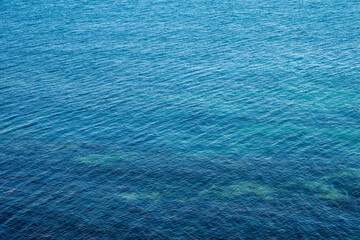 Gentle ripples dance across a blue sea, revealing subtle underwater textures and shifting light.