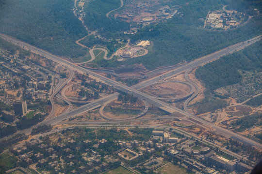 Aerial view of an intricate cloverleaf interchange where broad highways meet, contrasting with the surrounding dense green forests and urban sprawl, Skardu, Gilgit Baltistan, Pakistan.