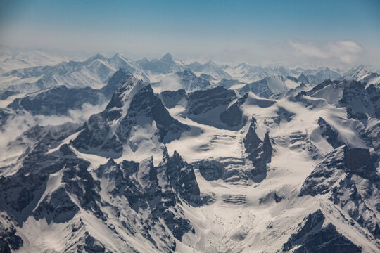 Aerial view of snow-capped jagged peaks pierce the sky, a symphony of white and grey under a serene blue canvas, Skardu, Gilgit Baltistan, Pakistan.