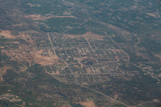 Aerial view of a planned community with geometric streets and scattered buildings nestled amidst rugged terrain and sparse vegetation, Skardu, Gilgit Baltistan, Pakistan.