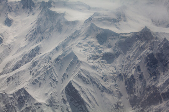 Aerial view of majestic, snow-laden mountains piercing through a blanket of clouds, their jagged peaks and frosted slopes creating a stark, wintry panorama, Skardu, Gilgit Baltistan, Pakistan.