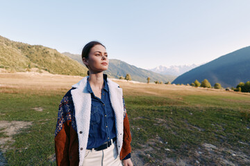 Fototapeta premium Woman portrait in mountains and nature on a valley field, wearing a jacket and denim shirt for travel and outdoors lifestyle, thoughtful pose with scenic horizon and sunlight.