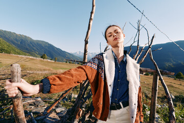 Fototapeta premium woman portrait in countryside mountains, fashion model leaning on wooden fence, rural lifestyle and outdoor clothing with relaxed expression and scenic natural landscape backdrop
