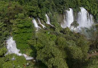 Aerial view of cascading waterfalls plunging amidst the verdant, dense forests, creating a symphony of rushing water and vibrant greenery, Cao Bang, Cao Bang, Vietnam.