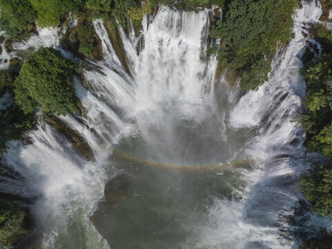 Aerial view of a powerful waterfall cascading down, creating a misty spray and a faint rainbow amidst the lush greenery, Cao Bang, Cao Bang, Vietnam.