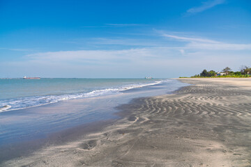 Wide, tranquil view of a tropical beach in Banjul, Gambia, featuring dark, rippled sand, small breaking waves, and clear blue sky