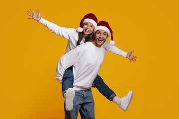 Playful couple shares a joyful moment wearing Santa hats. They appear energetic and happy, with one...