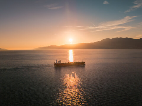 Aerial view of a tanker ship gliding across the tranquil Adriatic Sea under a radiant sunset near distant mountains, Rijeka, Primorje-Gorski Kotar County, Croatia.