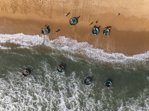 Aerial view of coracle boats resting on the golden sands where the turquoise sea meets the shore, Quy Nhon, Binh Dinh, Vietnam.