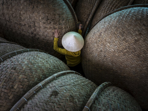 Aerial view of a person wearing a traditional conical hat amidst a sea of woven baskets, creating a textured landscape of light and shadow, S&ocirc;ng Cầu, Ph&uacute; Yen, Vietnam.