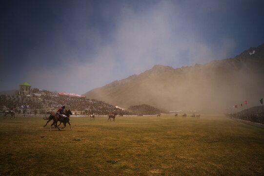 Shandur, Pakistan - 31 July 2017: View of a thrilling polo match amidst a cloud of dust, spectators lining the stands against the majestic backdrop of the mountains.