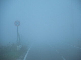 朝の濃霧の天気の中の道路と速度制限の印の様子