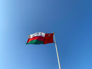 A large Omani flag flutters in the wind against a blue sky background. Oman flag waving in the wind.