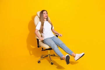 Young woman sits in a cream office chair on a bright yellow background expressing casual stylish...