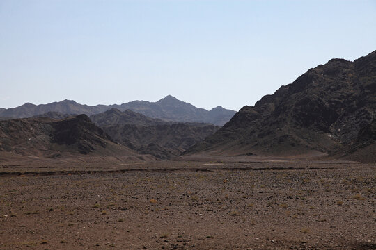 View of rugged, rocky terrain under a pale sky, the stark landscape defined by dark, mountainous silhouettes against the horizon, Quetta, Balochistan, Pakistan.