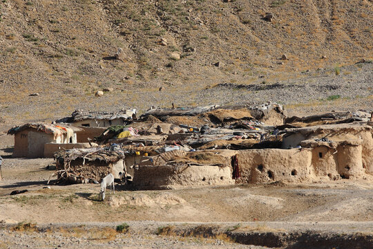 View of sun-baked mud houses clustered tightly together, their roofs a patchwork of straw and earth, nestled beneath barren hills, Quetta, Balochistan, Pakistan.