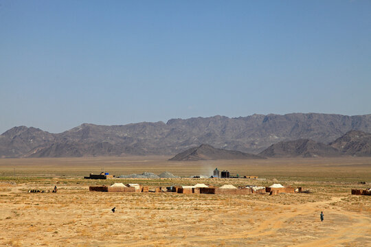 View of a parched landscape dotted with modest dwellings under a vast sky, mountains looming afar, a scene of resilience and stark beauty, Quetta, Balochistan, Pakistan.