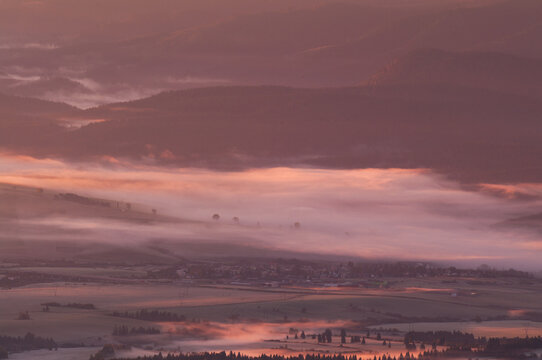 Aerial view of dawn's gentle blush paints the landscape, caressing the mountain peaks and veiling the village in a soft, ethereal mist, Western Tatras, Zillina Region, Slovakia.