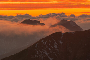 Aerial view of rugged peaks pierce a sea of clouds, painted in fiery hues by the setting sun, from Bystra, Zilina Region, Slovakia.