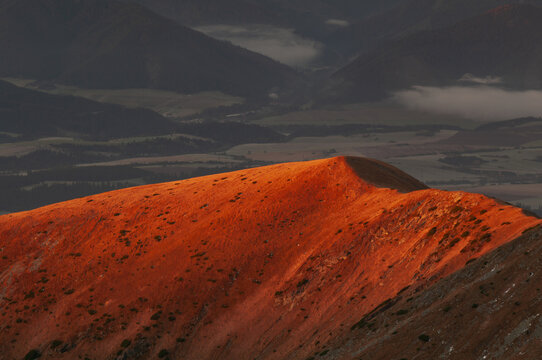 Aerial view of fiery sunlight igniting the peak of a rugged mountain ridge against the backdrop of shadowy valleys, from Bystra, Zilina Region, Slovakia.