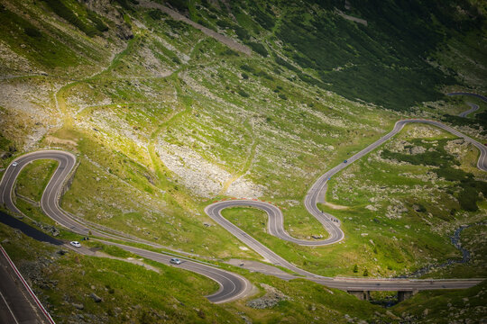 View of switchback roads cutting through vibrant green mountains, creating a stark contrast against the natural landscape, Poienari, Transilvania, Romania.