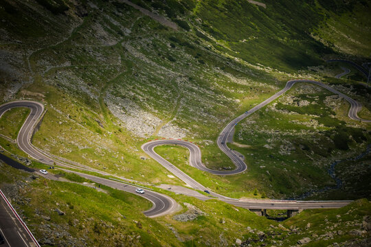 View of a winding road cutting through vibrant green mountainsides under the sun's embrace, a serpentine path, Poienari, Transilvania, Romania.
