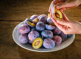 A person parts a ripe plum to show the inside while a plate overflows with more of the juicy fruit...