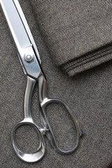 Close-up of sharp silver tailoring shears resting on folded gray and black wool tweed fabric with a classic, highly detailed herringbone weave. Perfect for professional tailoring and sewing.