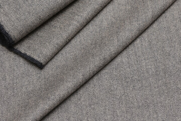Close-up view of classic English tweed wool fabric in a fine gray and black herringbone weave. Detailed texture and folded pattern perfect for tailoring suits, coats, and blazers.