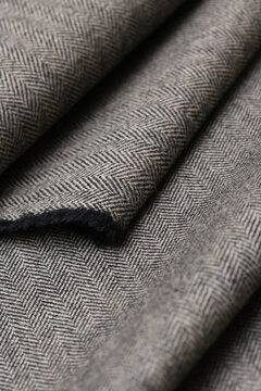 Close-up view of classic English tweed wool fabric in a fine gray and black herringbone weave. Detailed texture and folded pattern perfect for tailoring suits, coats, and blazers.