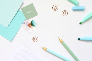 A visually appealing flat lay of pastel-colored stationery items arranged on a white surface. The composition includes two ballpoint pens with gold tips in mint green and light blue.