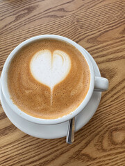 A cup of cappuccino with heart-shaped latte art served on a wooden tablet