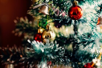 A close-up view of a decorated Christmas tree featuring shiny ornaments including a gold bauble, red baubles, and a small silver bell with a ribbon.