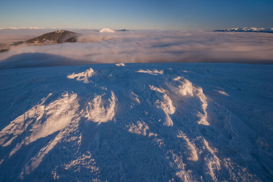 View of a snow-covered landscape meets a sea of clouds under a bright sky, accentuating the crisp winter air, Velka Hola, Banska Bystrica Region, Slovakia.