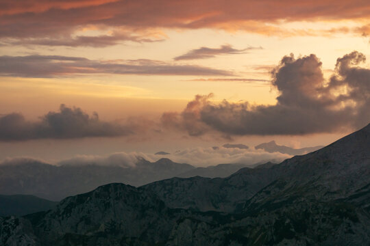 Aerial view of the rugged peaks of Tosc under a dramatic sky painted with fiery hues of orange and purple, Triglavski narodni park, Gorenjska, Slovenia.