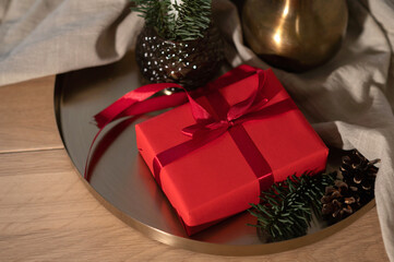 Red gift box with bow, pine cones on golden tray on table, holiday presents concept, Christmas celebration at home