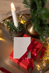 Red gift box and blank paper postcard or gift tag mockup, candle light and pine tree branch on table, Festive holiday background, celebration and presents concept, soft focus